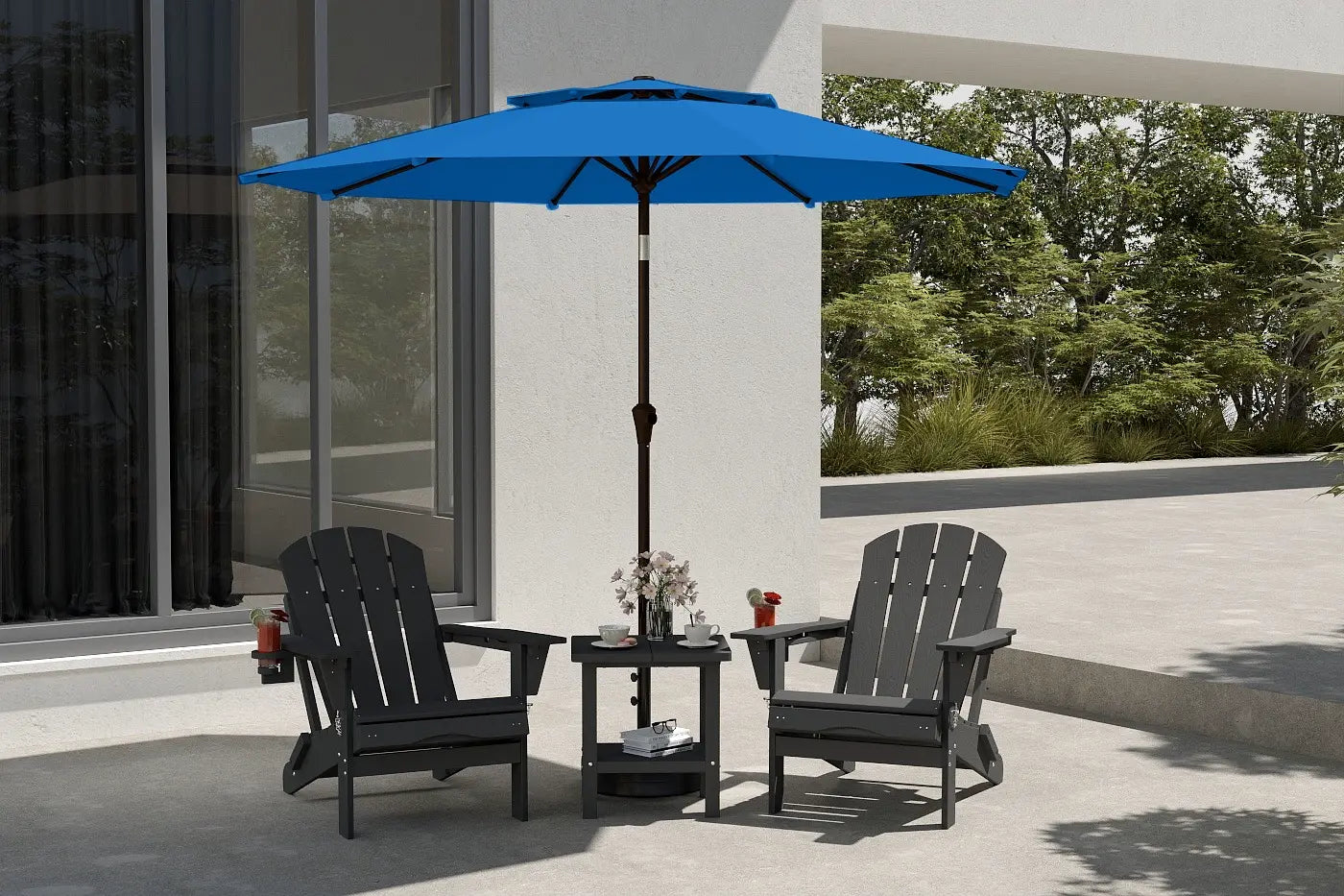 Blue patio umbrella over two black chairs on a patio with a white wall and greenery in the background.