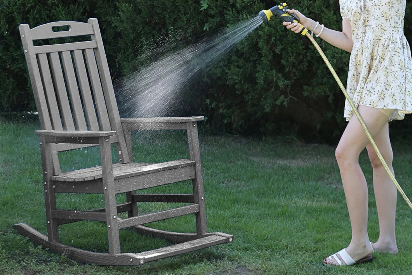 Person cleaning a wooden rocking chair with a hose outdoors.