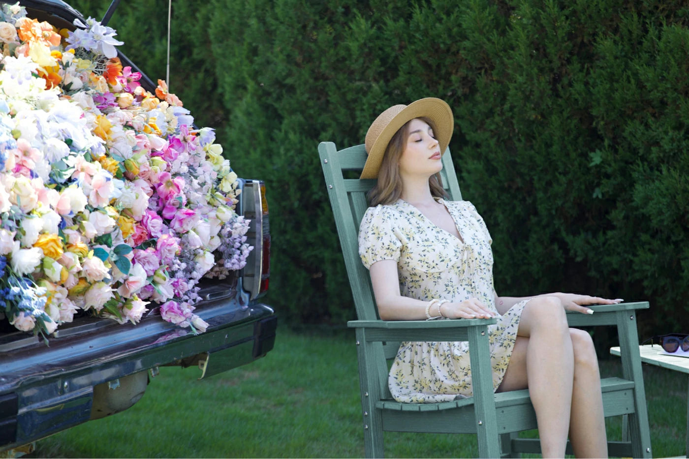 Woman in a floral dress sitting in a chair next to a truck filled with flowers outdoors.