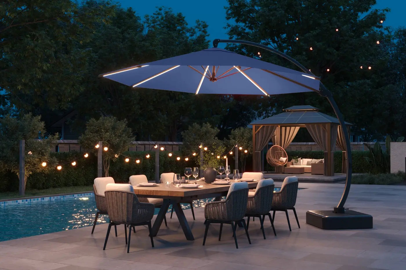 Outdoor dining setup with a large umbrella over a table by a pool at night.