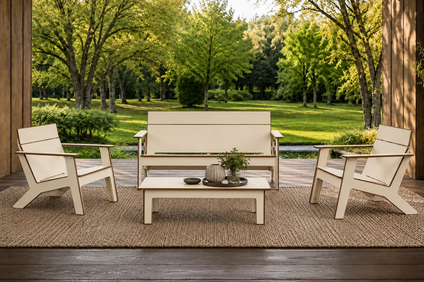 A coordinated outdoor patio furniture set including a loveseat, two armchairs, and a low rectangular coffee table, arranged on a woven rug in front of a porch with a lush green park background.