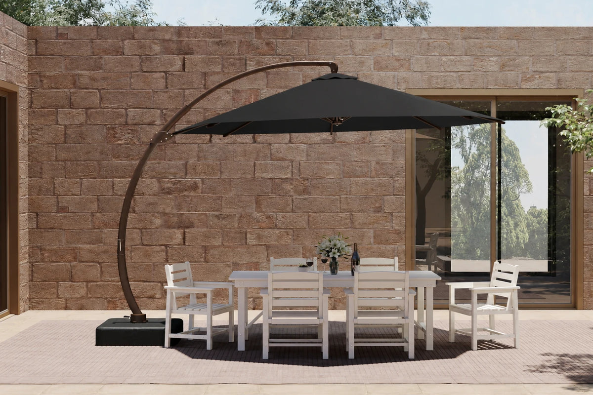 A large outdoor patio setup featuring a black cantilever umbrella over a white dining table and six matching chairs, set against a stone wall background.