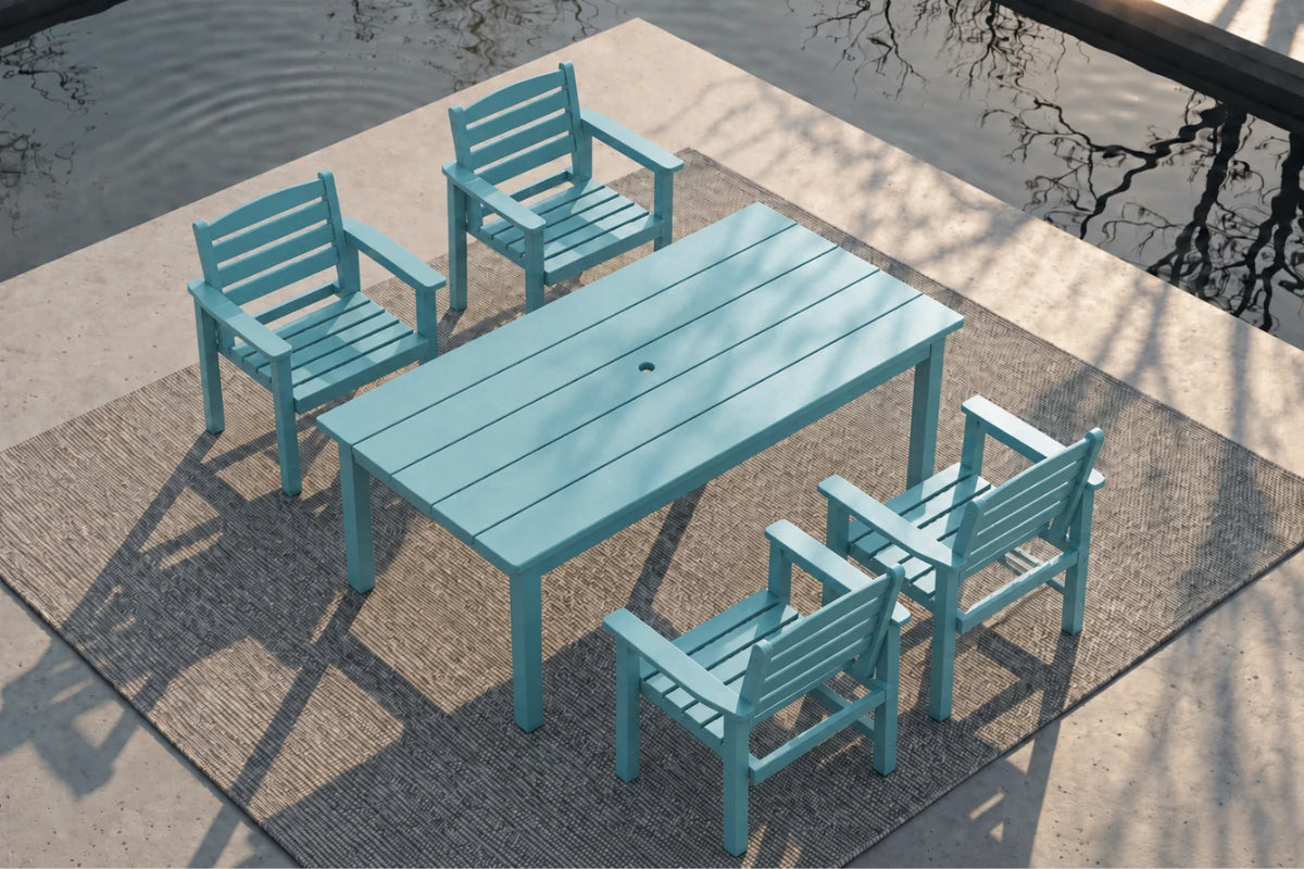 An Aruba blue outdoor dining set consisting of a rectangular slatted table and four matching armchairs, arranged on a woven rug beside a concrete patio and water.