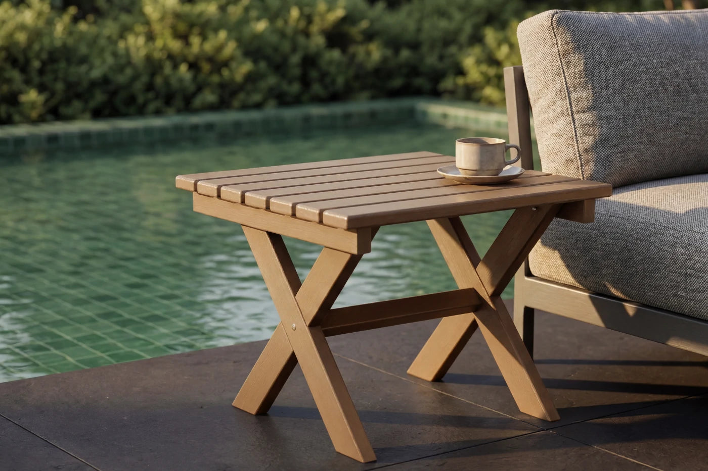 HDPE outdoor table with a cup and saucer next to a gray sofa by a pool.