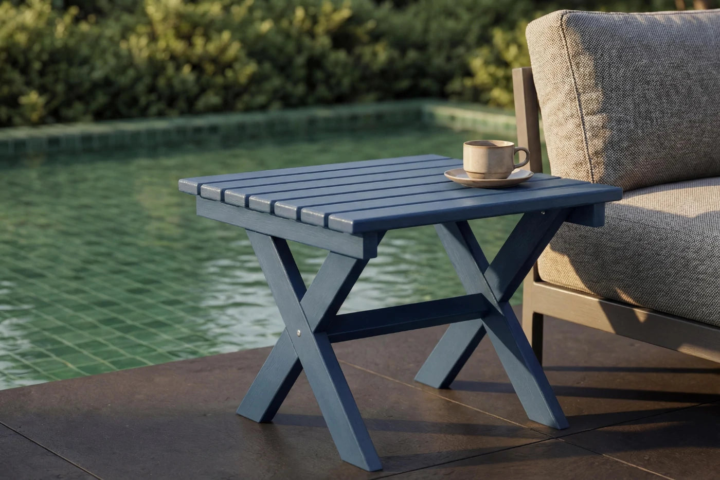 Outdoor side table with a cup and saucer next to a poolside chair.