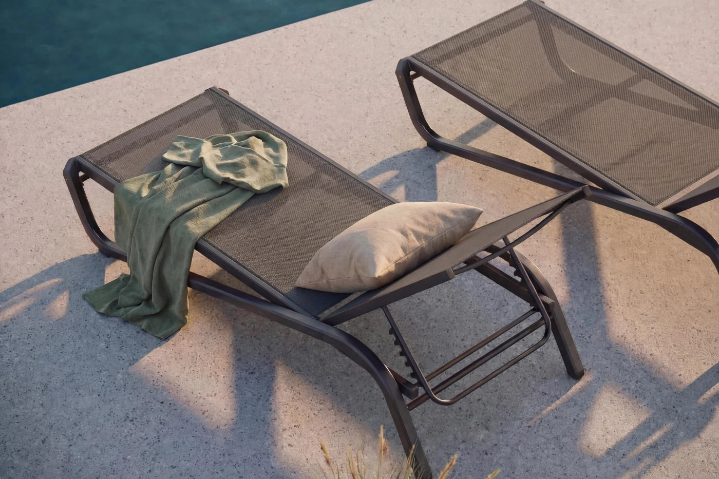 Two lounge chairs with a towel and pillow by a poolside.