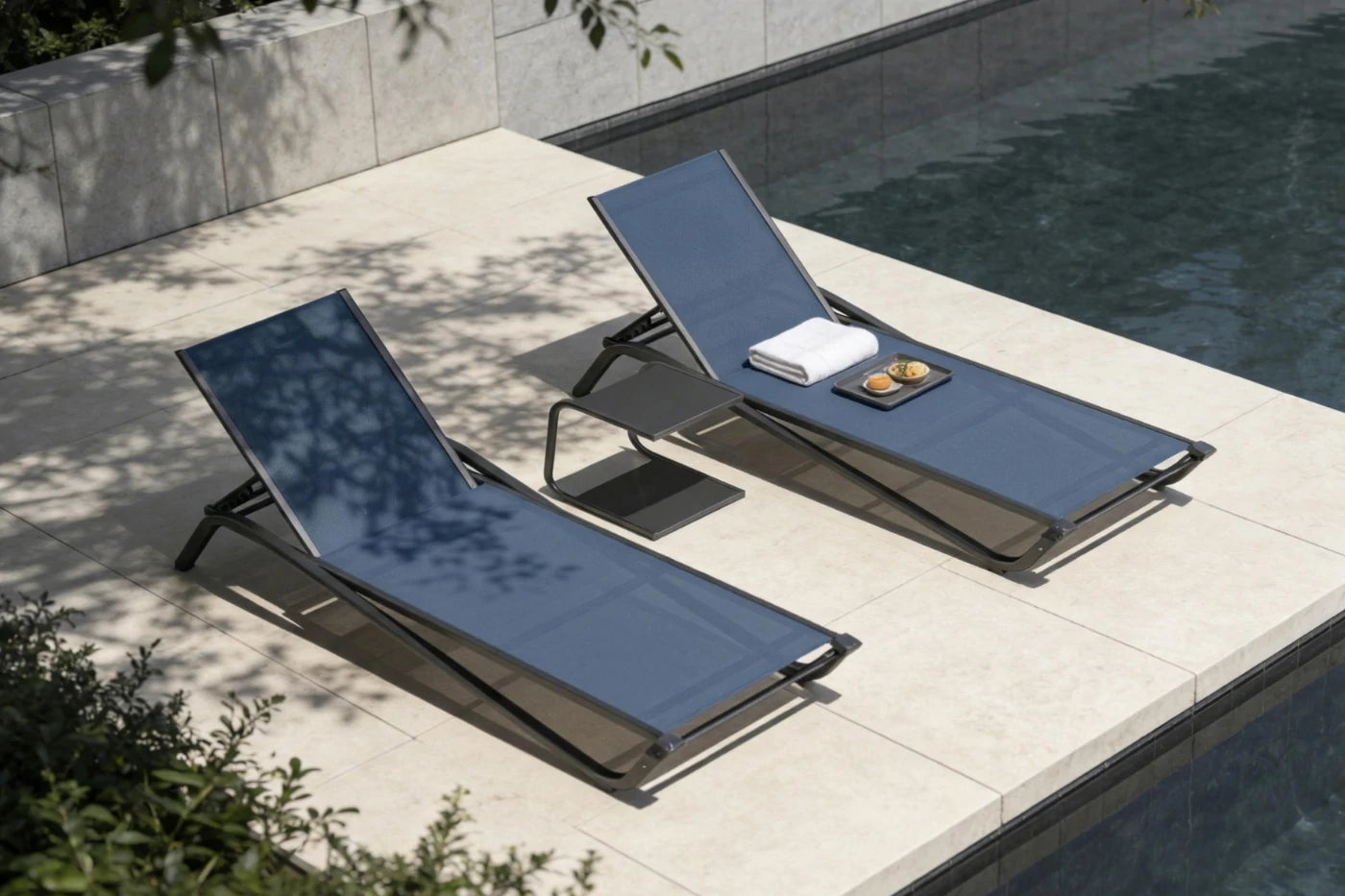 Two blue lounge chairs by a poolside with a towel and small items on one of them.