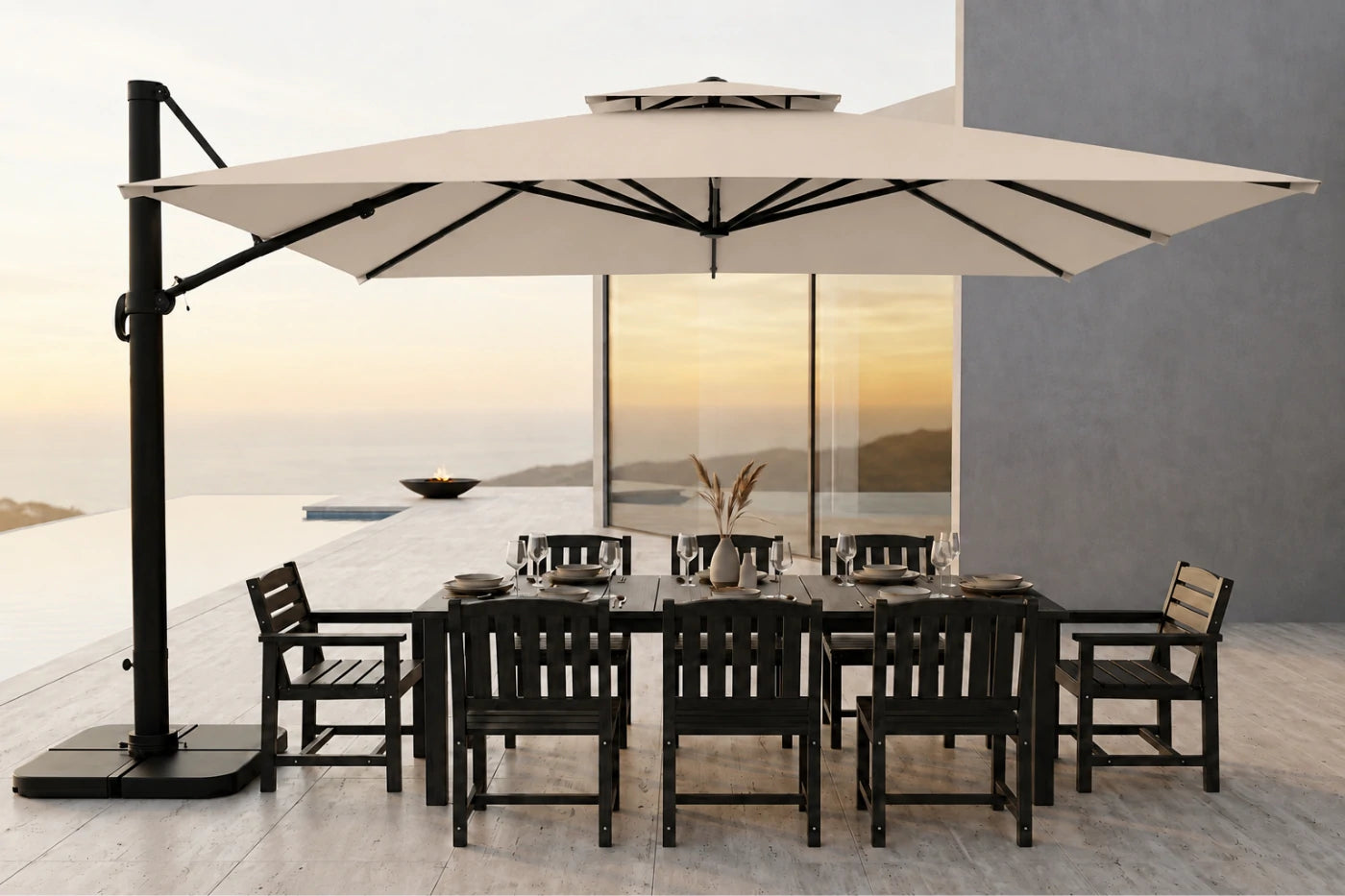 A large beige cantilever patio umbrella with a black metal frame is shown over a dark outdoor dining table and chairs on a modern terrace at sunset.
