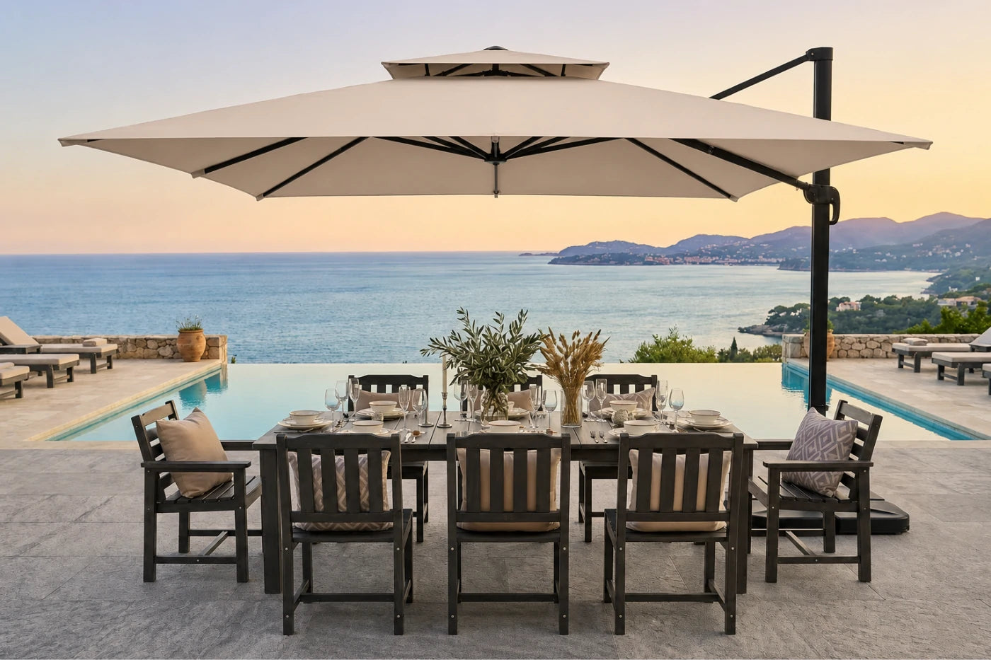 Outdoor patio dining set with a rectangular dark wood table, matching slatted chairs, a large beige patio umbrella, and a pool overlooking the sea at sunset.
