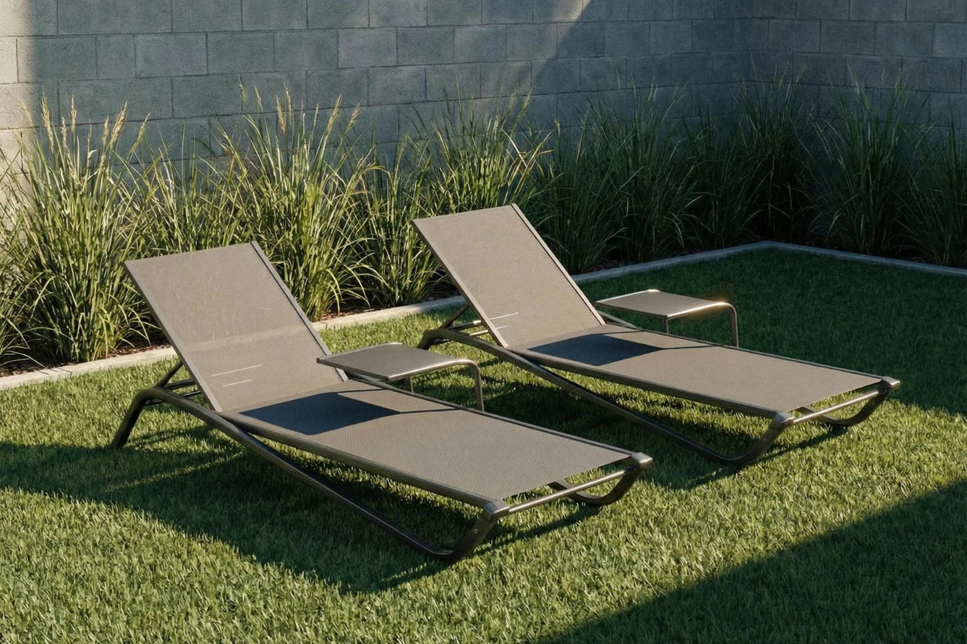 Two beige lounge chairs on grass with a stone wall and plants in the background