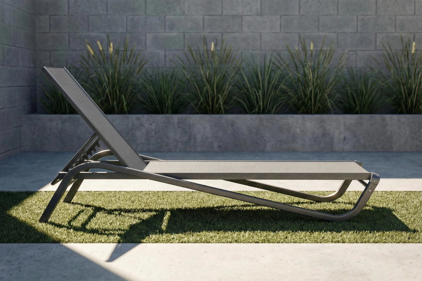 Modern outdoor lounge chair on grass with a stone wall and plants in the background