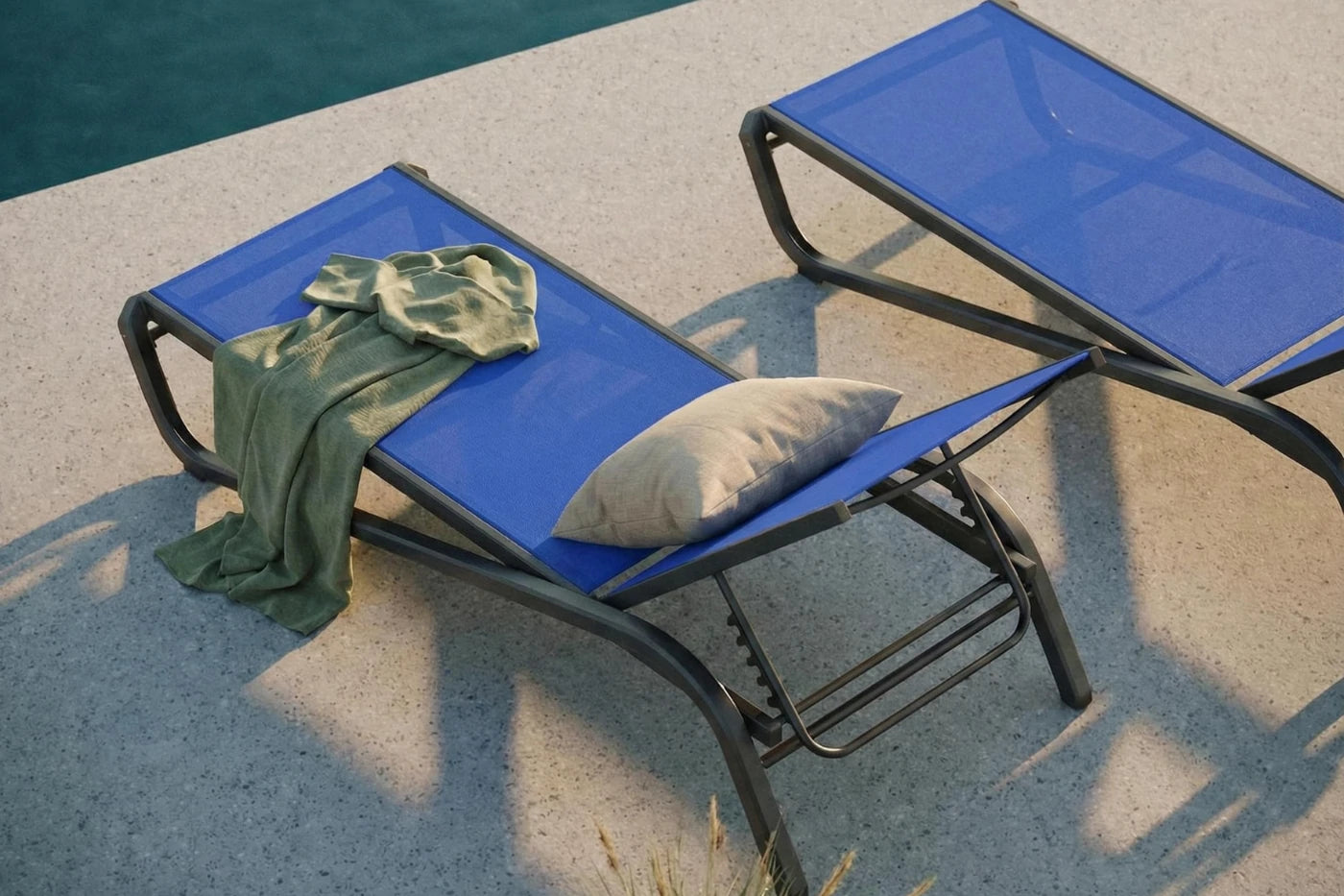 Two blue lounge chairs by a poolside with a towel and pillow on one of them.