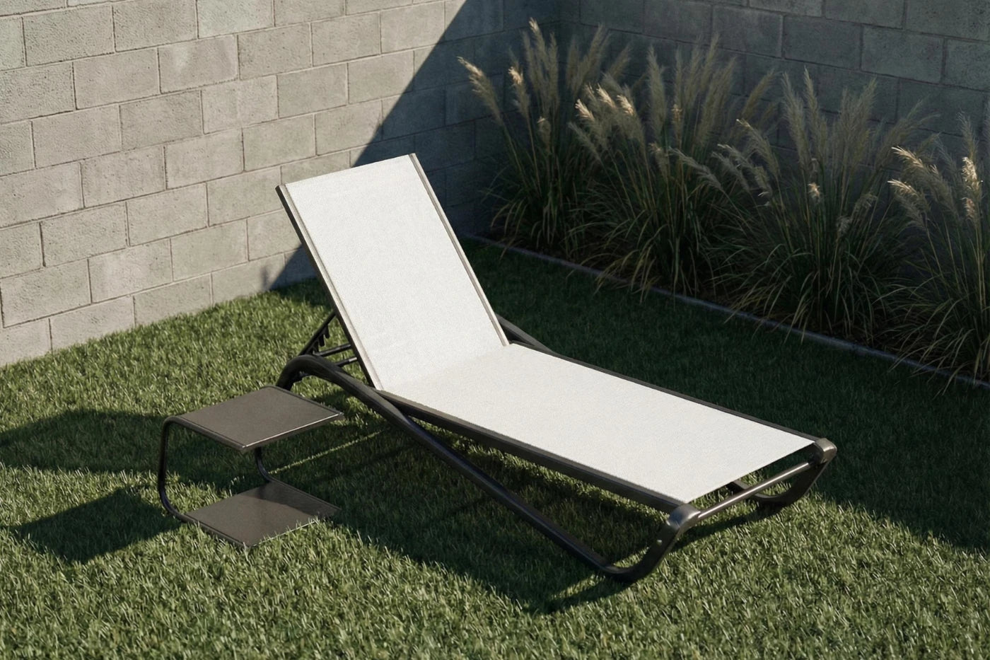 White lounge chair on grass with a stone wall and plants in the background