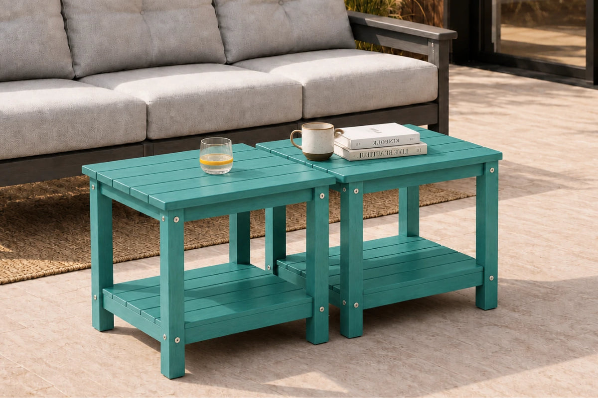 A teal outdoor nesting coffee table set with two tables and a lower shelf, styled in a patio living room setting with a gray sofa in the background.