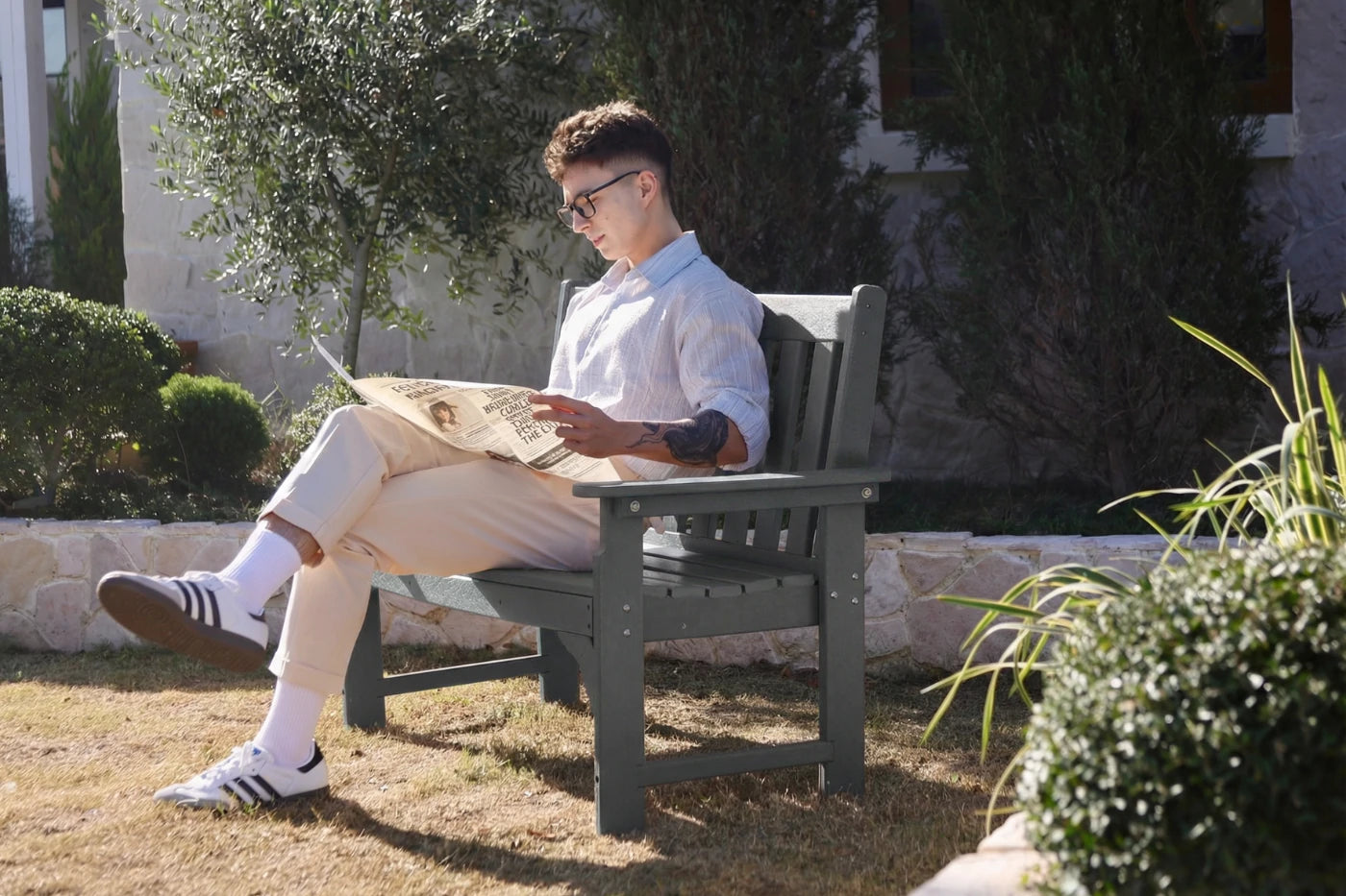 Man sitting on a bench reading a newspaper in a garden setting