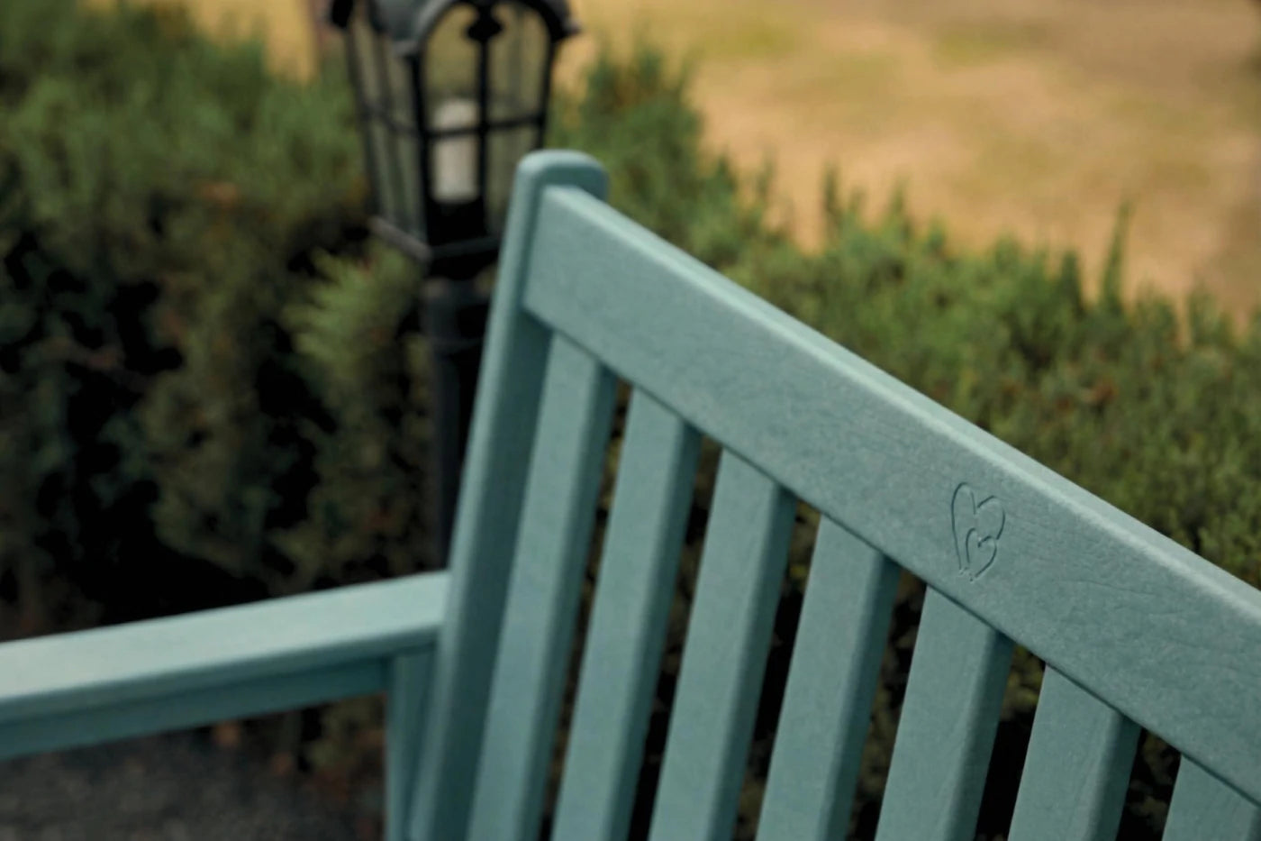 Teal bench with a blurred background of greenery and a lamp post.
