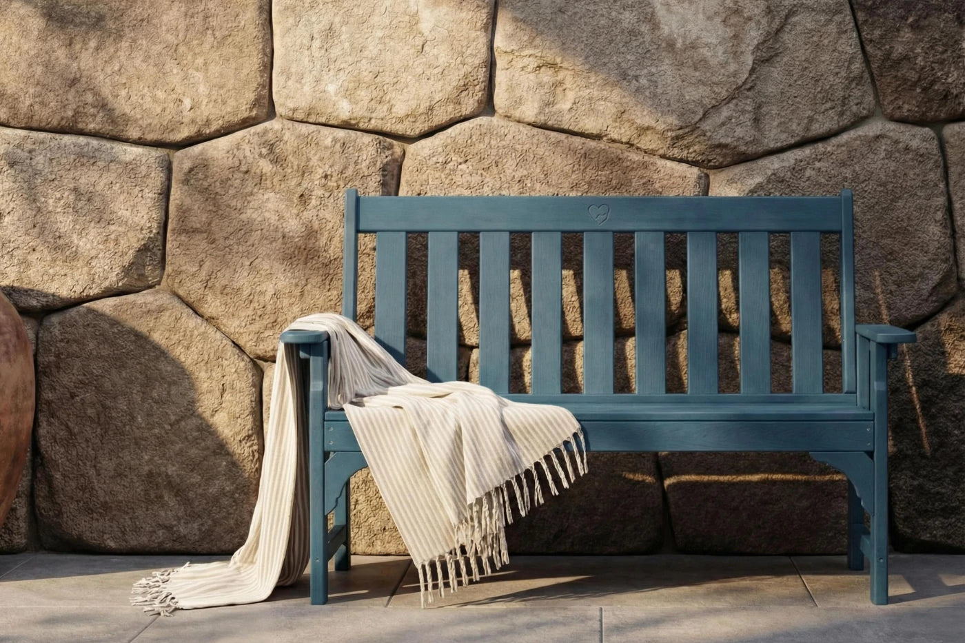 Blue bench with a blanket draped over it against a stone wall.