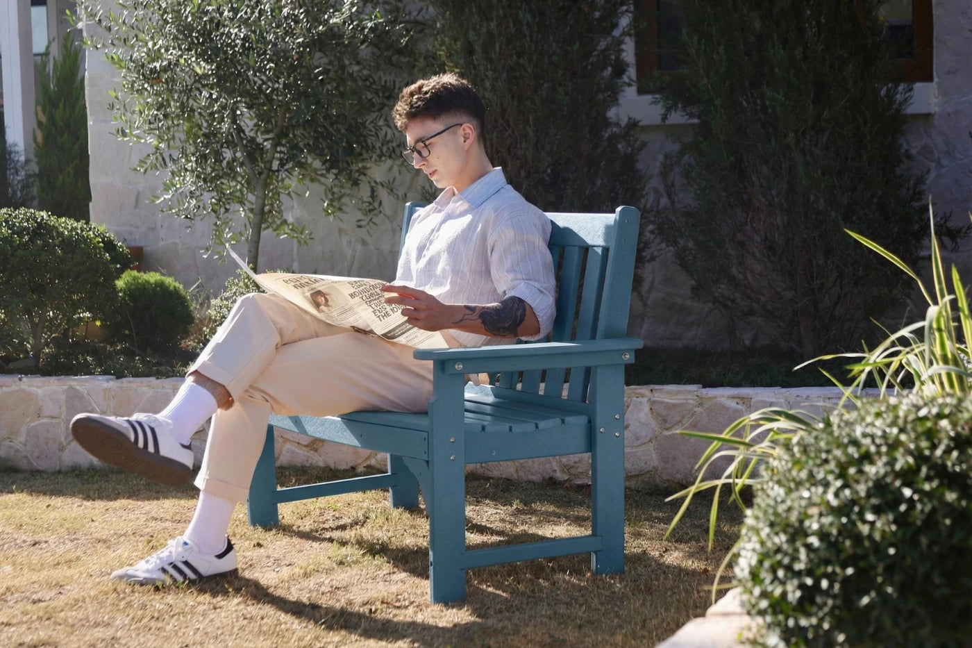 Man sitting on a blue bench reading a newspaper in a garden setting.