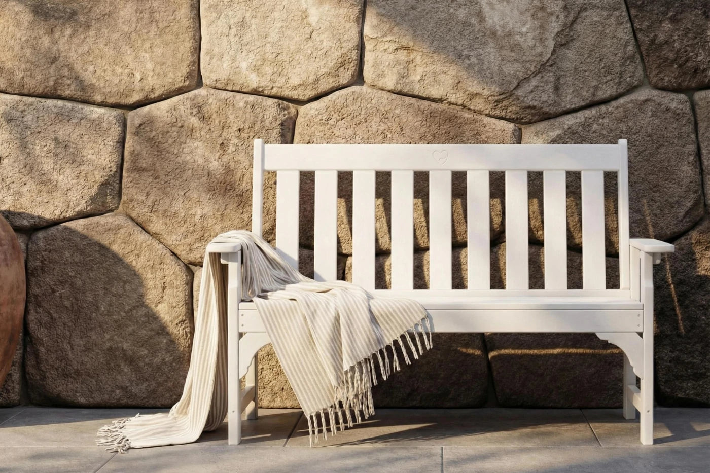 White bench with a blanket draped over it against a stone wall.