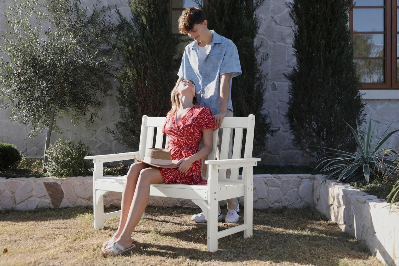Two people sitting on a white bench in a garden setting.