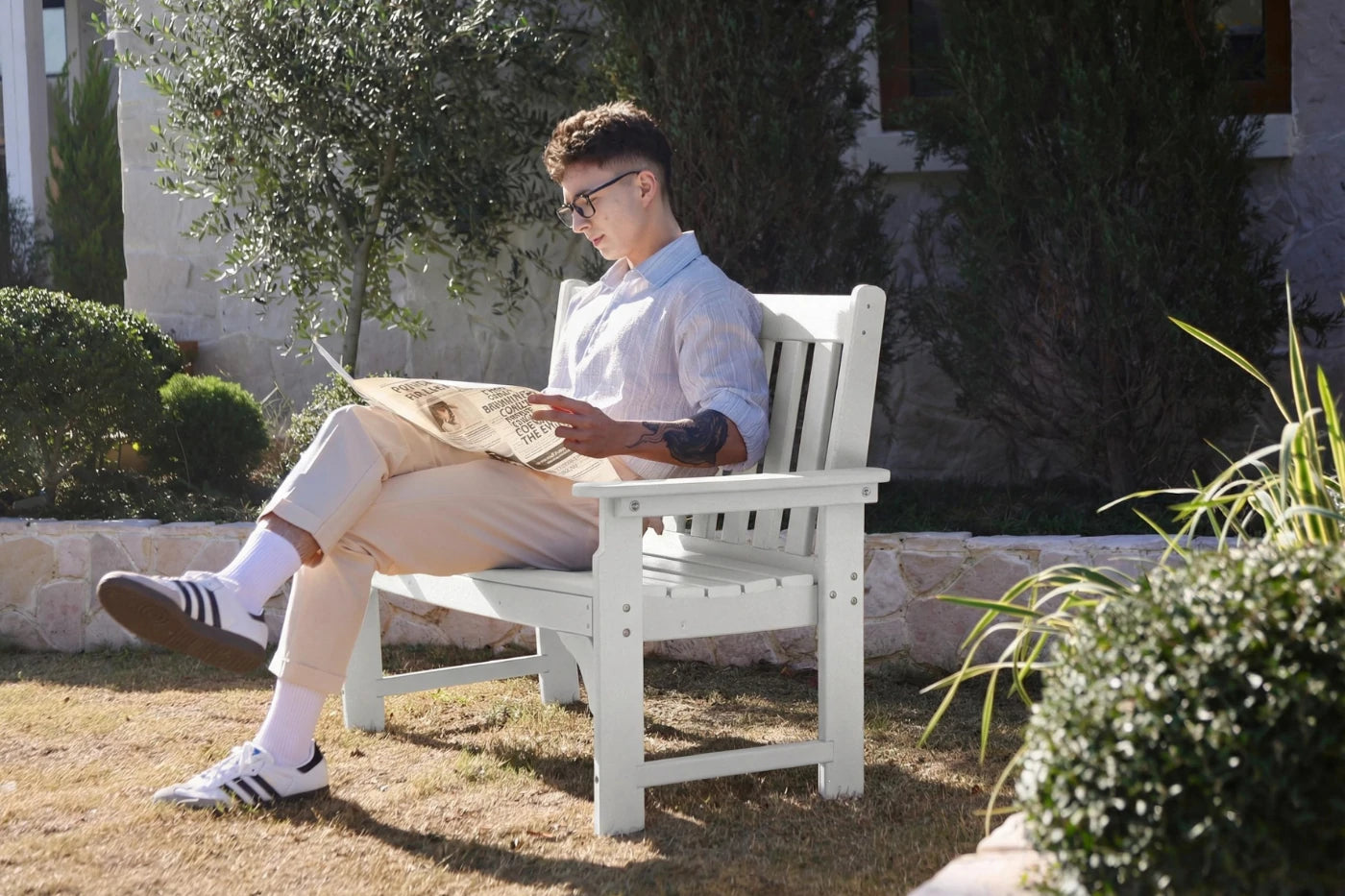 Man reading a newspaper on a white bench outdoors