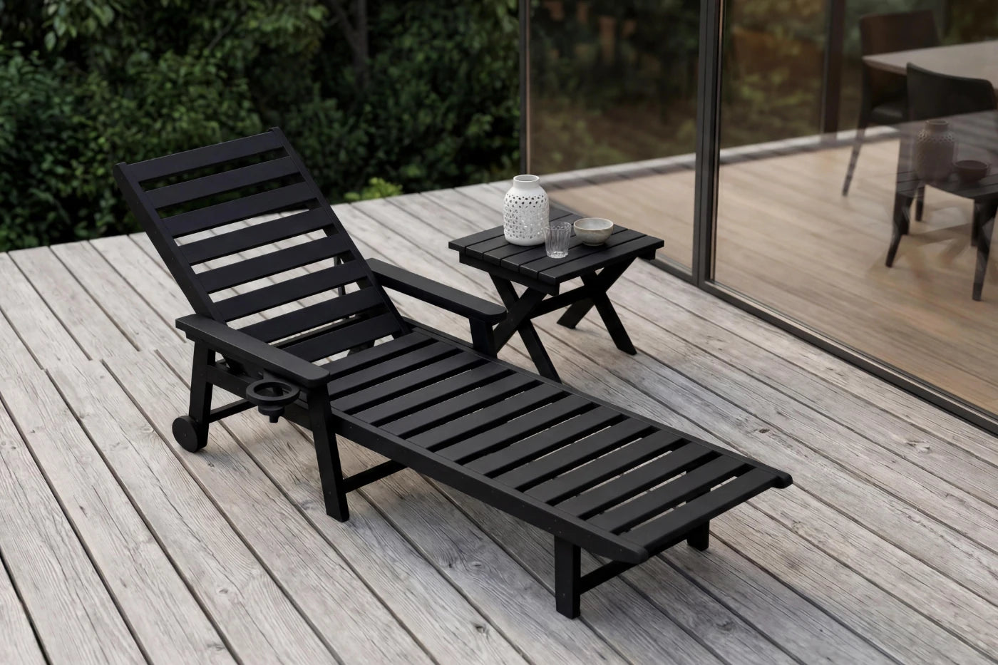 Black lounge chair and side table on a wooden deck with outdoor furniture in the background.