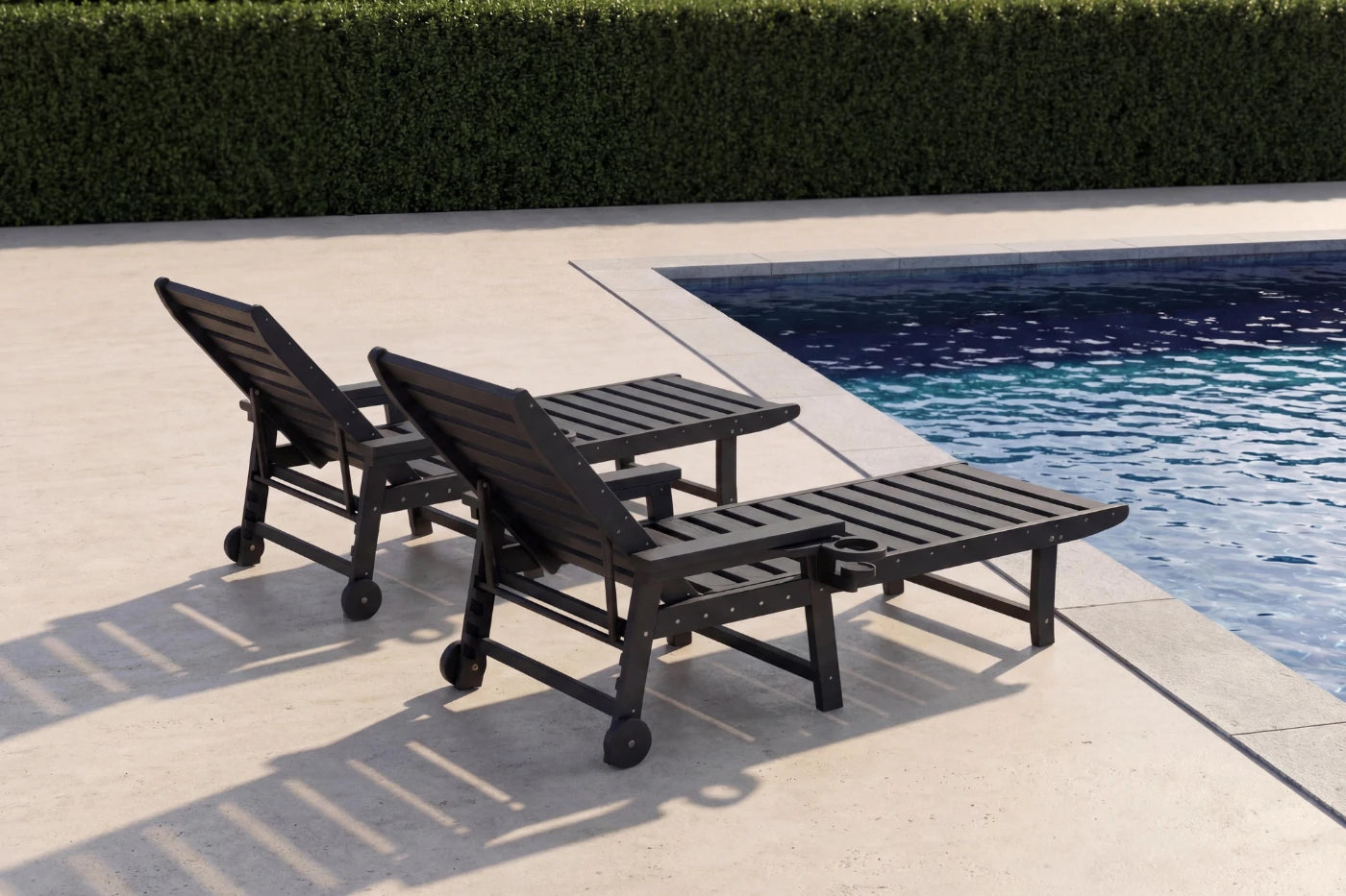 Two black lounge chairs by a poolside with a hedge in the background
