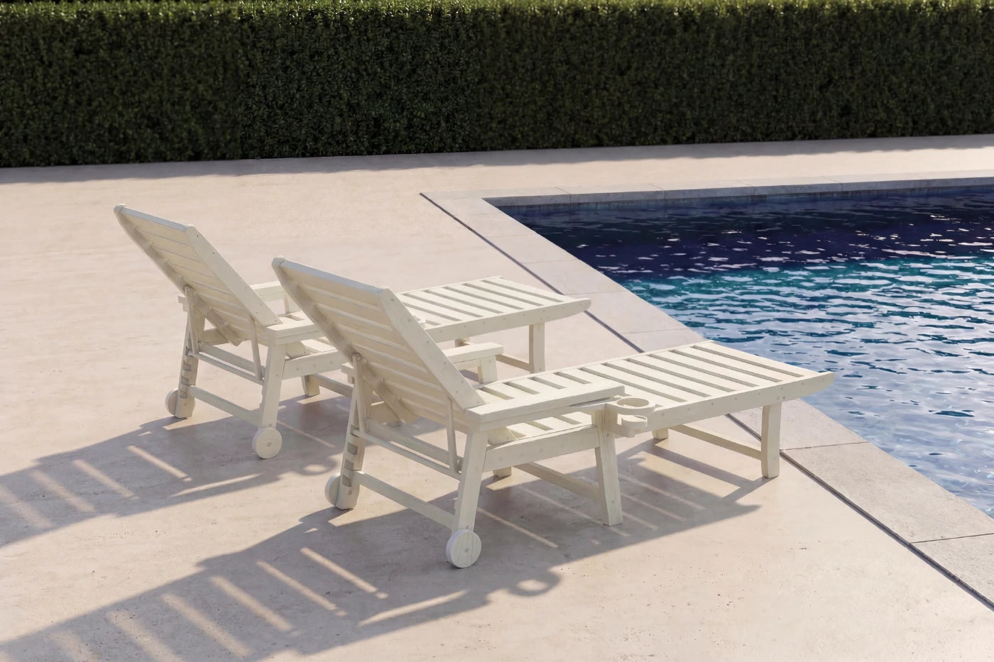 Two white lounge chairs by a pool with a hedge in the background