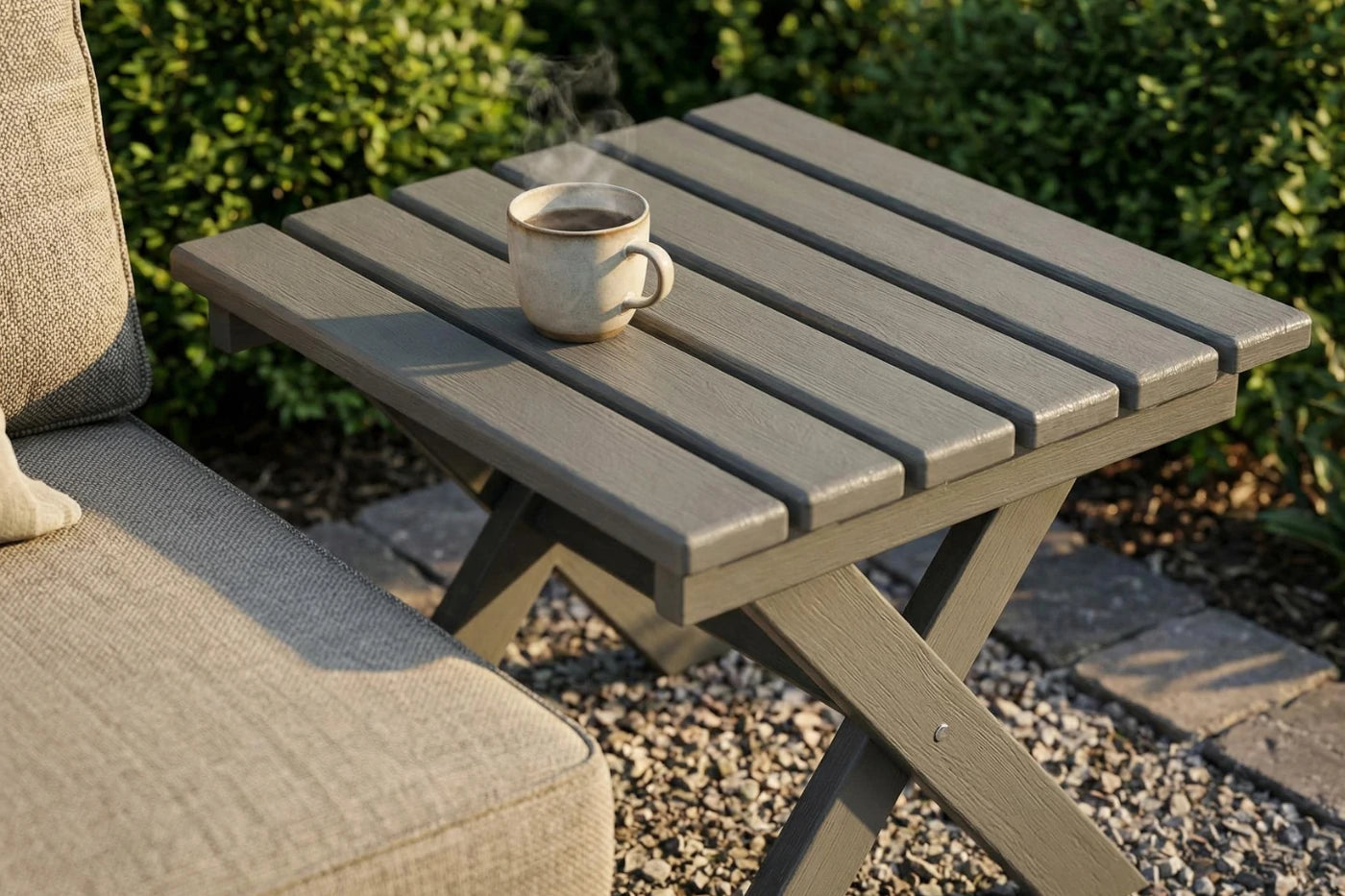 Small outdoor table with a cup of steaming coffee next to a cushioned chair.