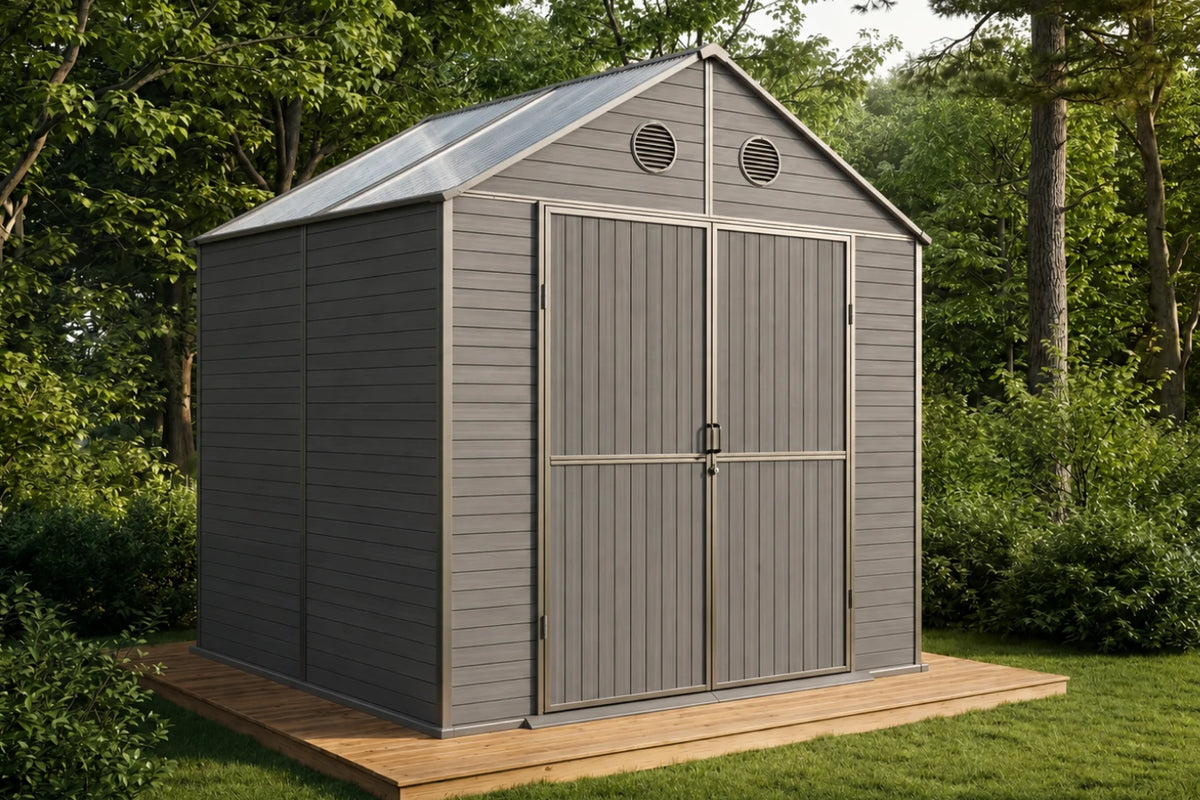 A gray resin storage shed with double doors and a polycarbonate roof, shown on a wooden deck in a grassy backyard with trees.