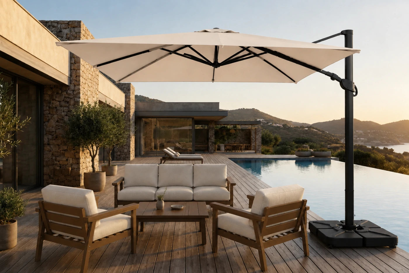 A large beige patio umbrella with a black cantilever pole and weighted base, shading a modern outdoor lounge set with wooden chairs and a sofa on a poolside deck.