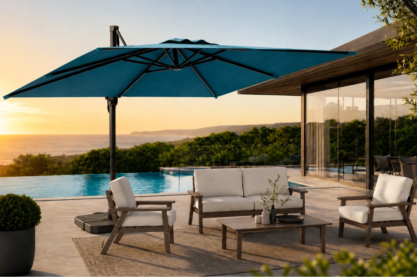 A large lake blue patio umbrella shading a modern outdoor seating area with a pool at sunset. The scene includes a sofa, two armchairs, a coffee table, and a house with glass walls in the background.