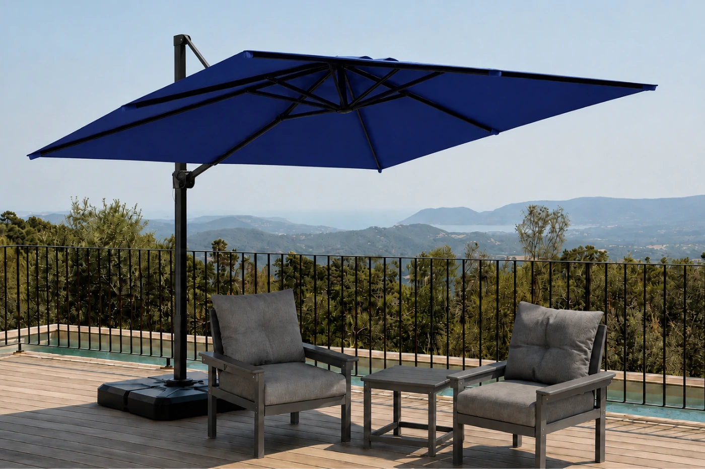 A large navy blue cantilever patio umbrella on a wooden deck with two gray lounge chairs and a small side table, overlooking a scenic mountain landscape.