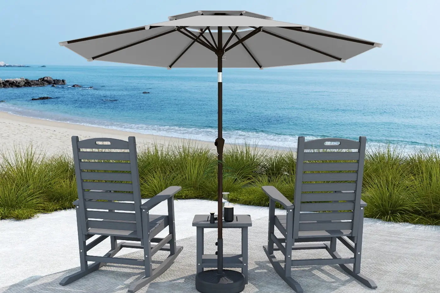 Two gray chairs with a matching table and umbrella on a sandy beach.