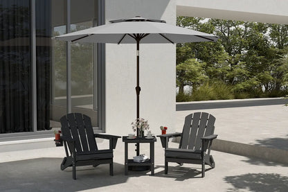 Two black Adirondack chairs with a small round table and umbrella on a patio.