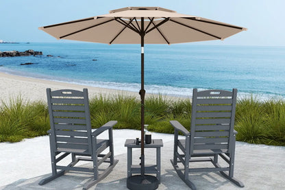 Two gray chairs with a small table and beige umbrella on a sandy beach.