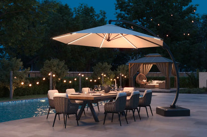 Outdoor dining setup with a large illuminated umbrella over a table by a pool at night.