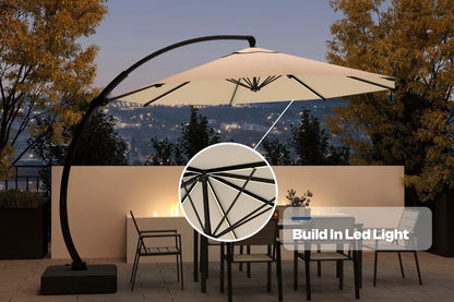 Beige patio umbrella with built-in LED light on a stand, set against a scenic background.