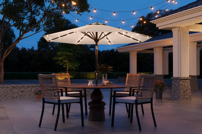 Outdoor patio set with table, chairs, and umbrella under string lights at night.