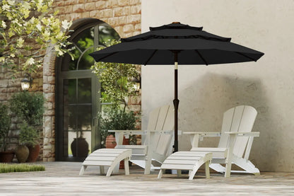Black patio umbrella over two white chairs in an outdoor setting with a stone wall and greenery.