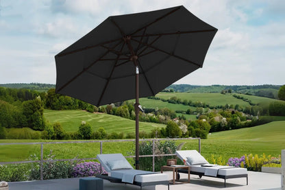 Black patio umbrella over lounge chairs with a scenic background of green fields and trees.