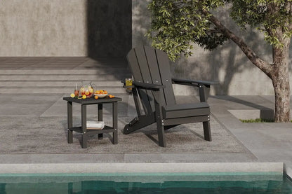 Black Adirondack chair and side table by a poolside with a tree in the background.