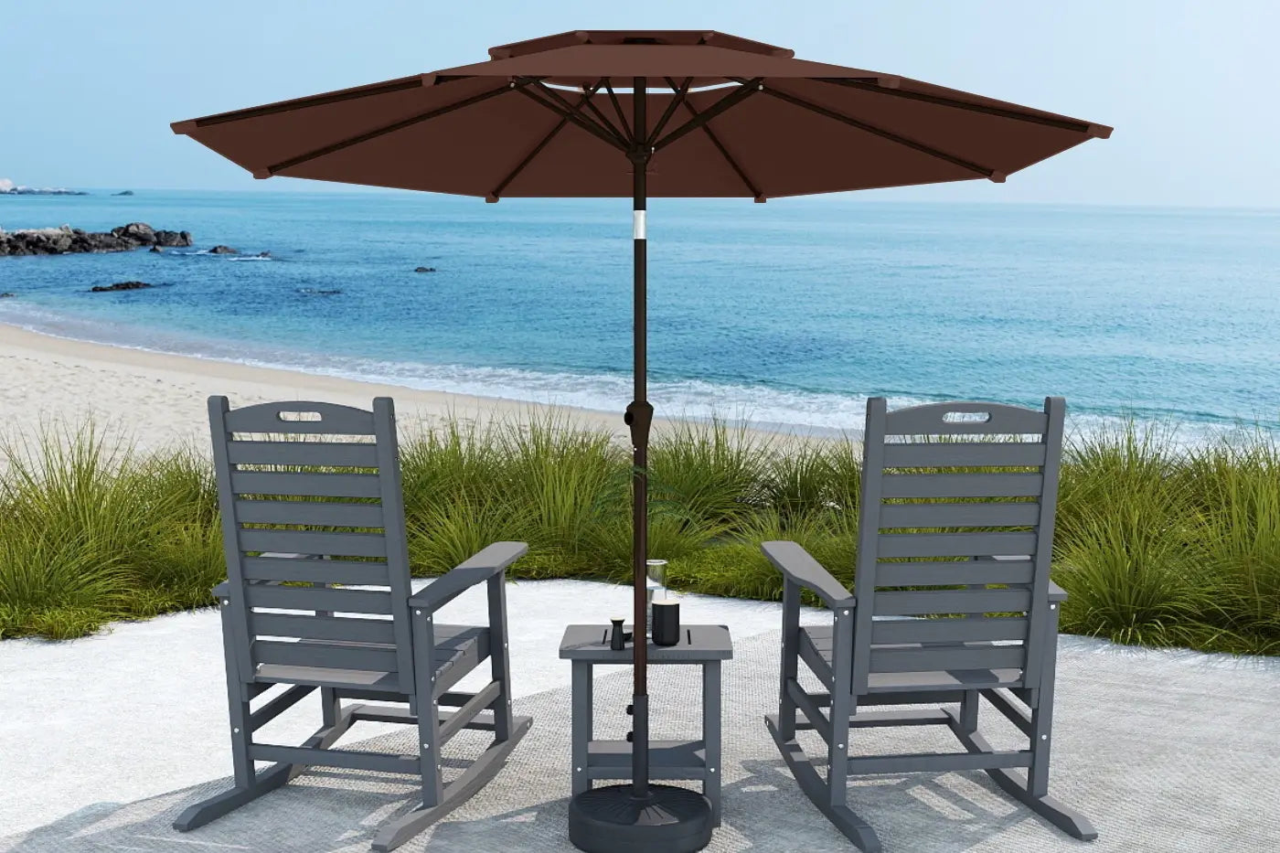 Two gray chairs with a table and brown umbrella on a sandy beach.