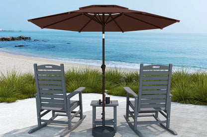 Two gray chairs with a table and brown umbrella on a sandy beach.