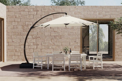 Outdoor patio set with white chairs and table under a large beige umbrella against a stone wall.