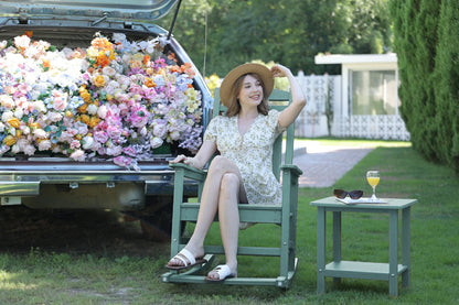 Woman sitting in a chair next to a car filled with flowers, with a table and sunglasses in the foreground.