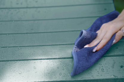 Hand using a blue microfiber cloth to wipe a green surface
