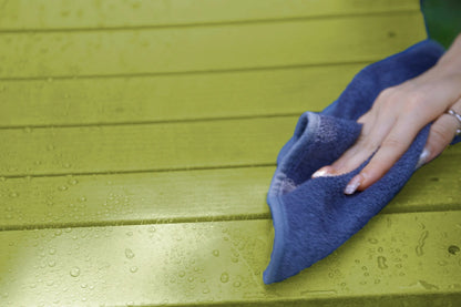 Hand using a blue cloth to wipe a green wooden surface