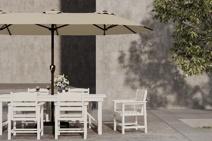 Outdoor dining setup with white table and chairs under a beige umbrella against a concrete wall.