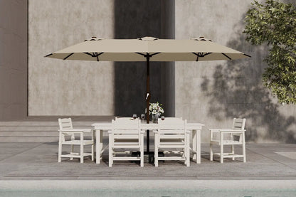 Outdoor dining set with a large beige umbrella on a wooden deck by a pool.